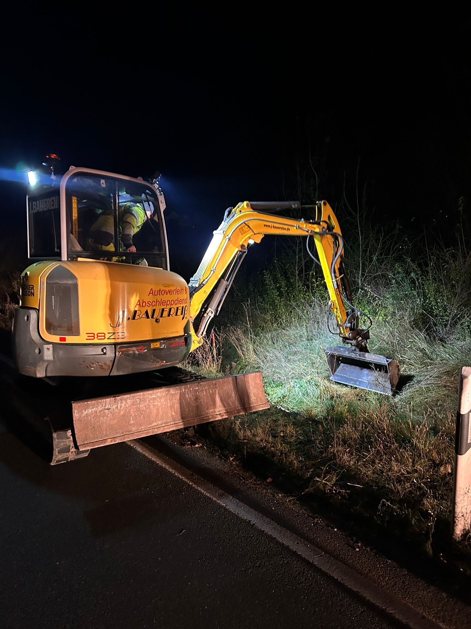 Ein gelber Bagger steht nachts am Straßenrand.