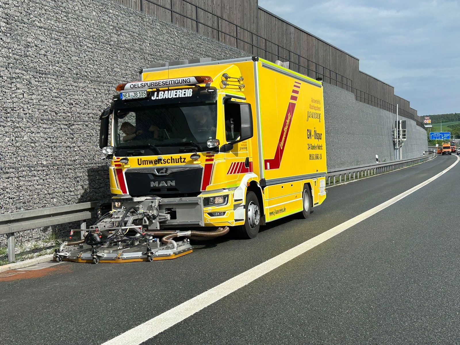 Ein gelber Lastwagen fährt auf einer Autobahn neben einer Steinmauer entlang.