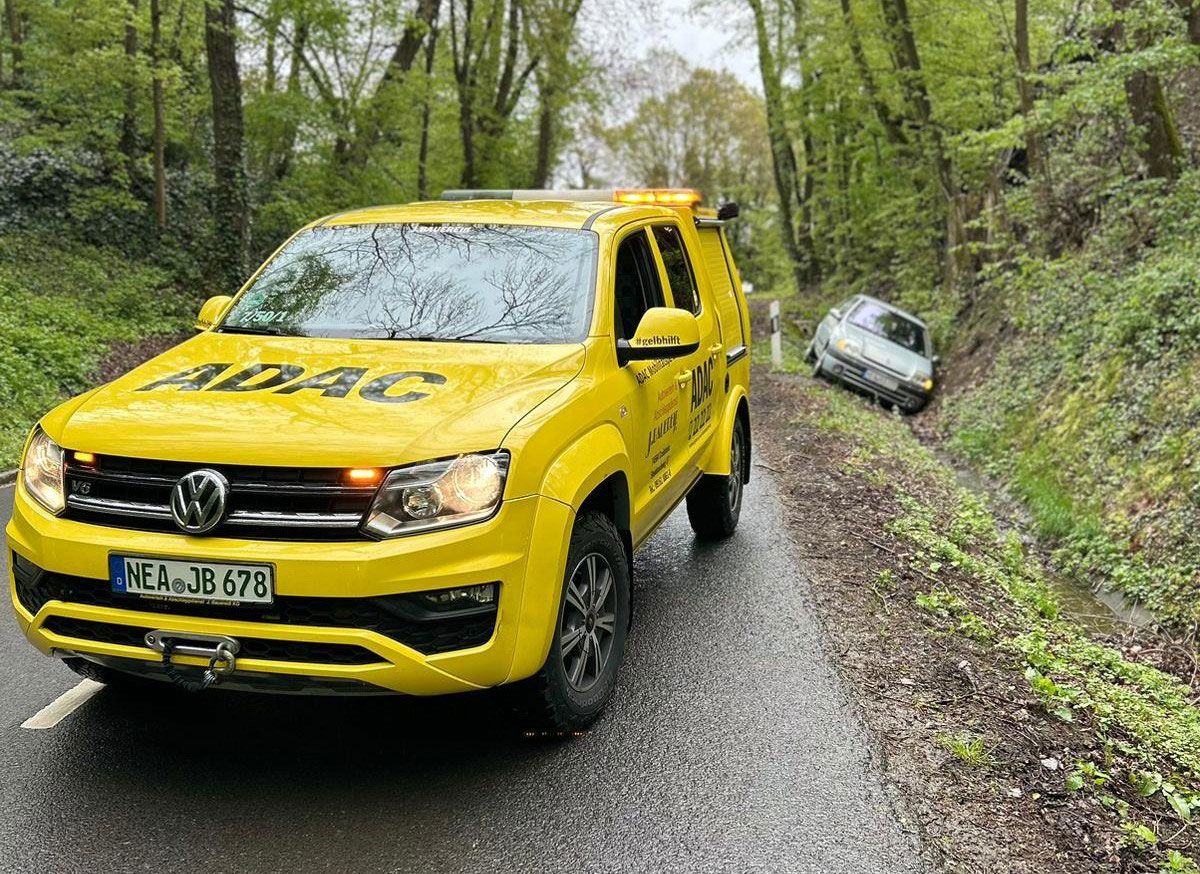 Ein gelber Lastwagen fährt eine Straße entlang, die an einem Wald entlangführt.