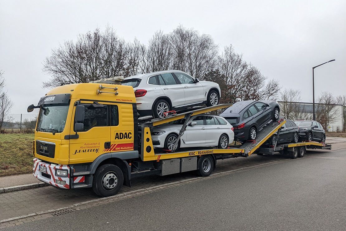 Auf dem Dach eines gelben Abschleppwagens sind mehrere Autos geladen.
