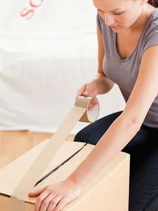 Una mujer está empacando una caja de cartón con cinta adhesiva.