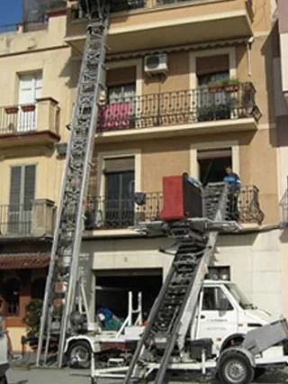 Un camión blanco con una escalera adjunta está estacionado frente a un edificio.