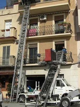 Un camión blanco con una escalera adjunta está estacionado frente a un edificio.