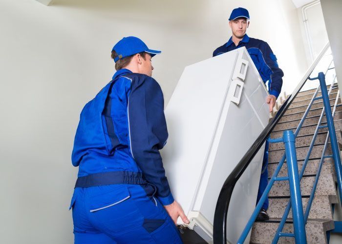 Dos hombres suben un frigorífico por unas escaleras.