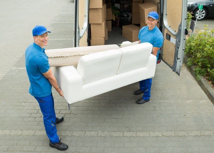 Dos hombres sacan un sofá blanco de una camioneta.