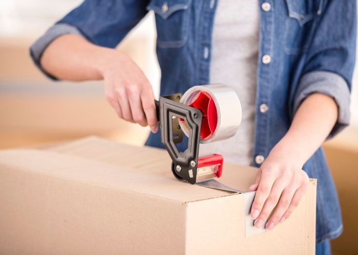 Una mujer está pegando una caja de cartón con cinta adhesiva.