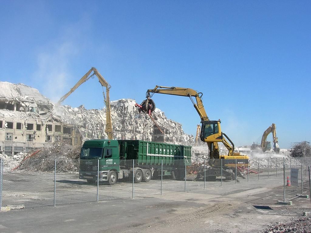 Chantier de démolition : des excavatrices démantèlent un bâtiment et chargent les débris dans un camion vert.