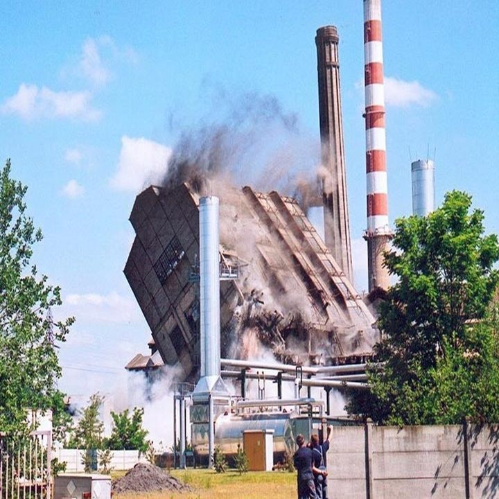 Démolition d'un bâtiment industriel avec des cheminées d'usine, fumée épaisse, deux personnes qui regardent.