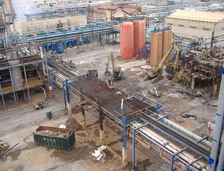 Site industriel avec canalisations, réservoirs et machines lourdes, possiblement en construction ou en démolition.