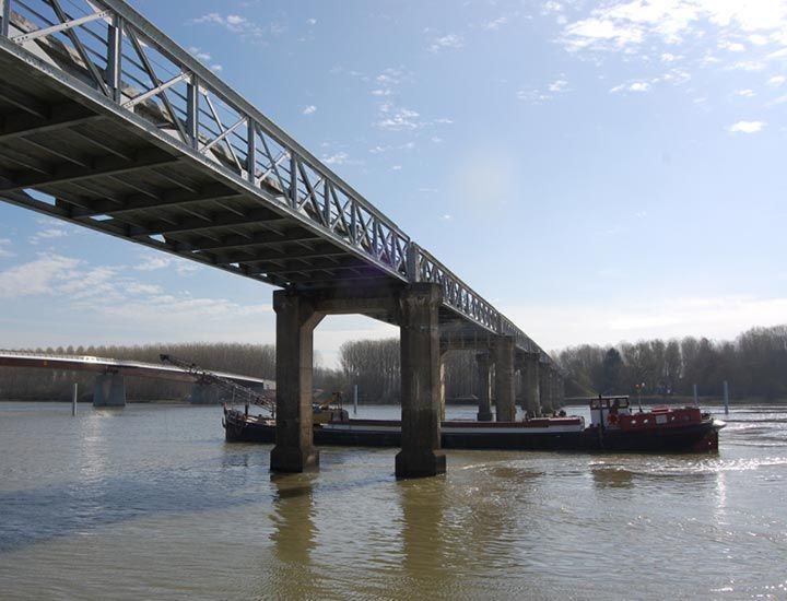Pont enjambant une rivière, avec une péniche passant en dessous par une journée ensoleillée.