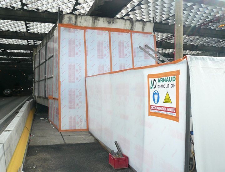 Chantier avec panneaux de protection blancs et orange, entrée de tunnel routier et panneau de sécurité.