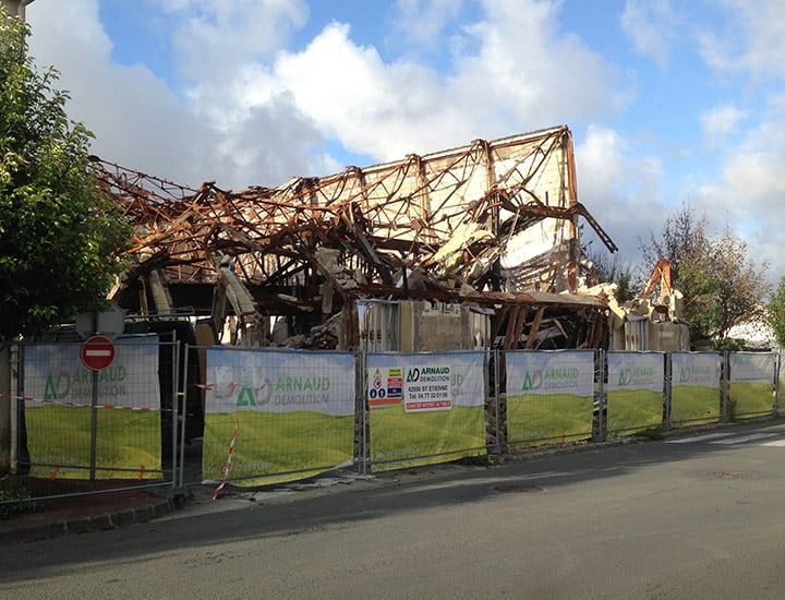 Bâtiment démoli derrière un chantier clôturé, dans une rue sous un ciel nuageux.