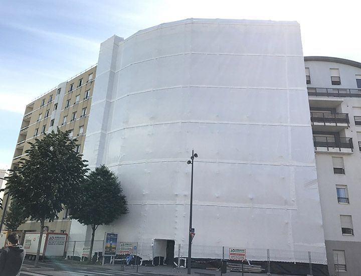 Façade du bâtiment recouverte d'une bâche de protection blanche pendant les travaux de construction ou de rénovation.