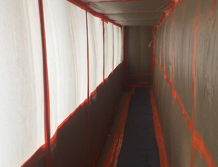 Vue intérieure d'un espace rectangulaire clos, recouvert de bâches en plastique et de ruban adhésif ; il s'agit probablement d'une zone de construction.