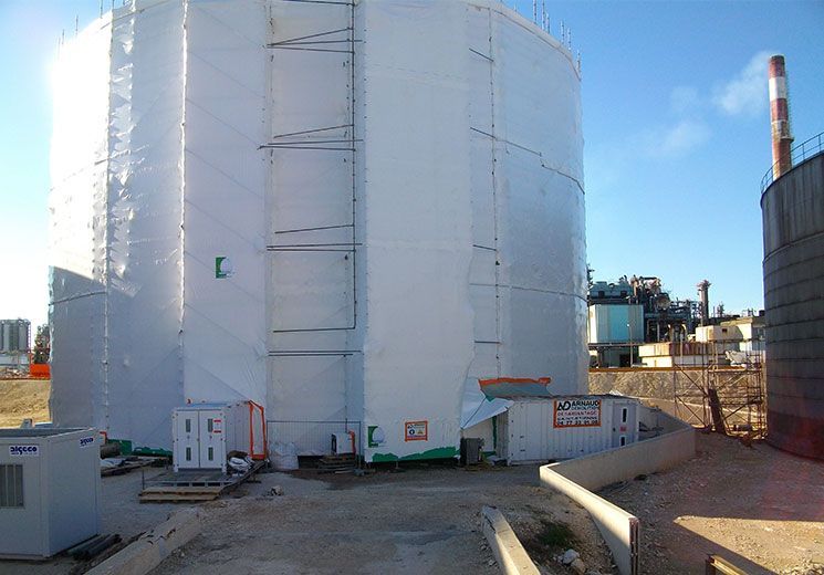 Grand réservoir de stockage blanc recouvert d'un matériau de protection sur un site industriel ; ciel bleu.