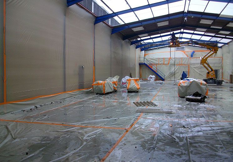 Intérieur d'un entrepôt en construction, recouvert de bâches en plastique et de ruban adhésif orange. Un monte-charge est en service.