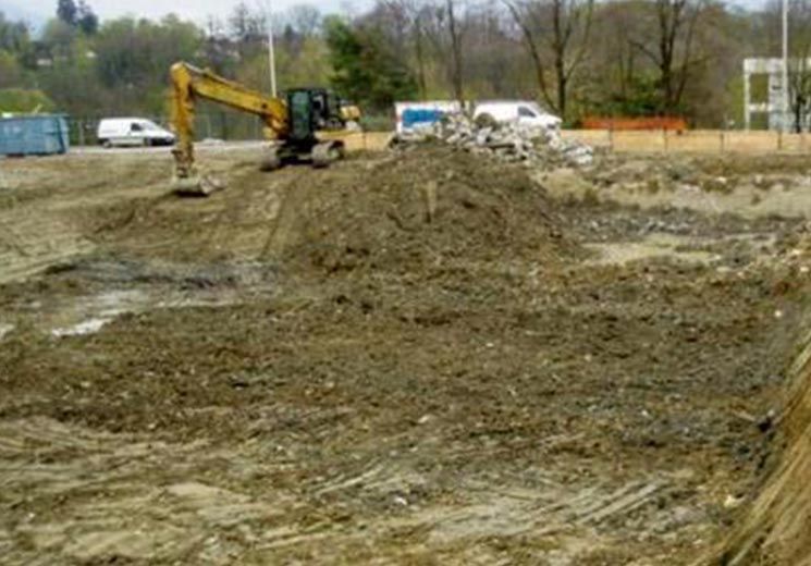 Pelleteuse mécanique sur un chantier, déplaçant terre et débris. Sol brun, ciel dégagé.