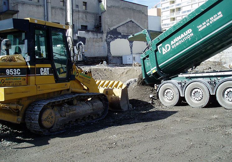 Un bulldozer jaune pousse de la terre dans un camion-benne vert sur un chantier de construction.