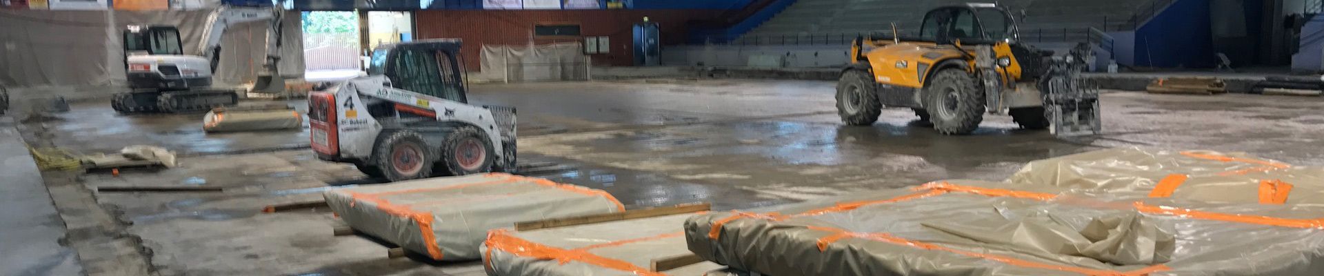 Chantier de construction avec plusieurs engins de chantier, dont une chargeuse compacte et un chariot élévateur.