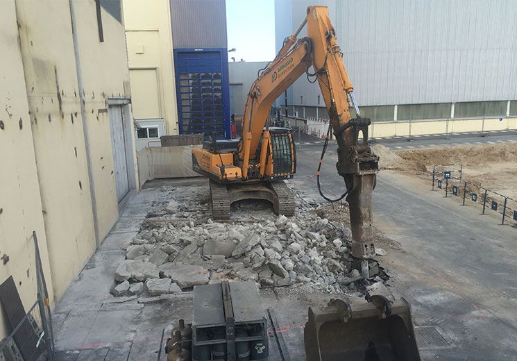 Une excavatrice équipée d'un marteau-piqueur démolit du béton près d'un bâtiment.