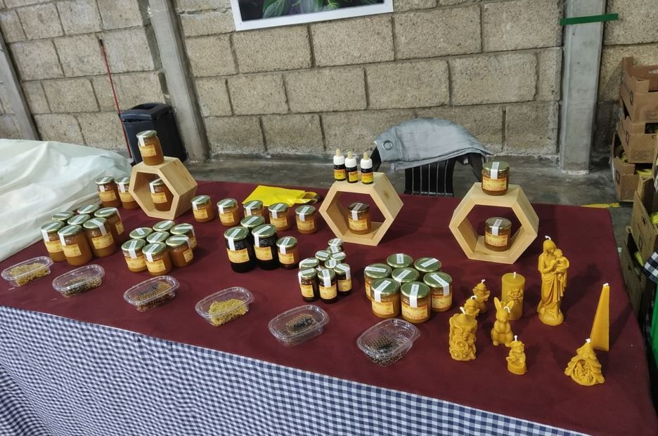 Una mesa expositora con varios tarros de miel, estantes de madera con forma de panal y velas decorativas de cera de abeja.