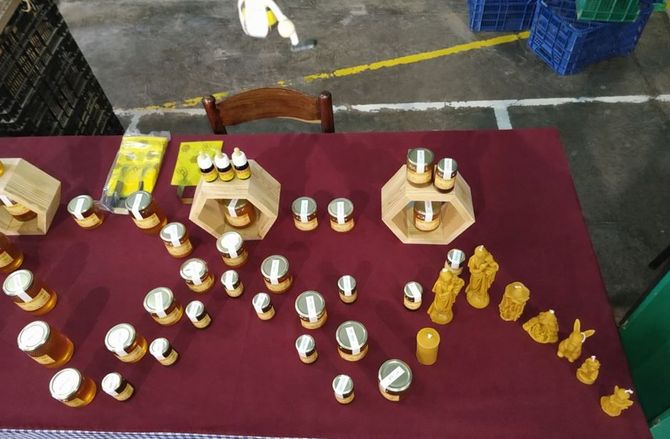 Productos de cera de abeja, como velas y tarros de miel, dispuestos sobre una mesa con un mantel granate en un evento.