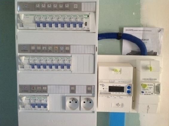 Panneaux de disjoncteurs et compteurs d'énergie fixés au mur avec des conduits bleus.