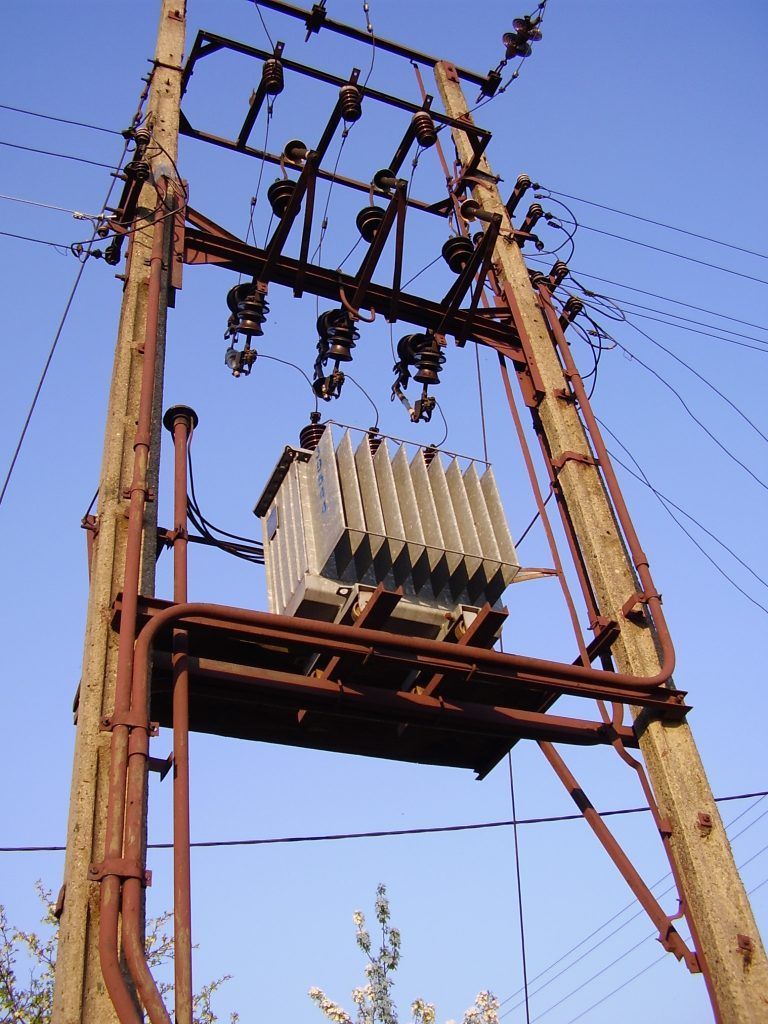 Transformateur électrique sur un poteau électrique se détachant sur un ciel bleu, avec lignes électriques aériennes et isolateurs.