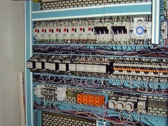 Panneau de commande électrique avec rangées de disjoncteurs, de relais et de câblage bleu.