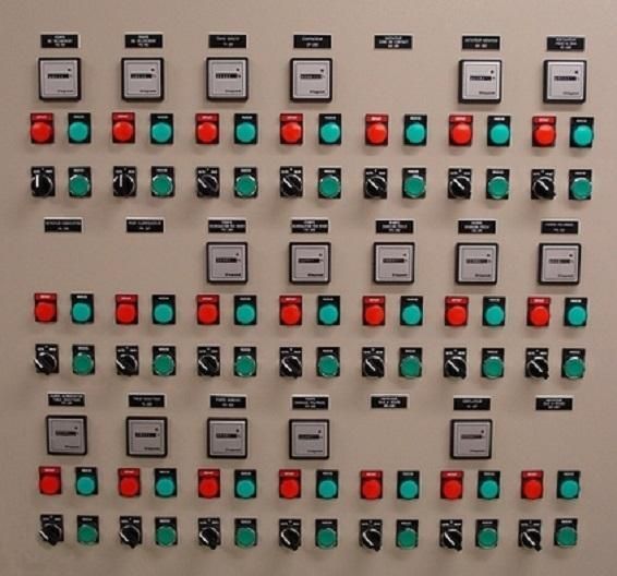 Panneau de commande électrique avec rangées de boutons rouges, verts et noirs et interrupteurs étiquetés.