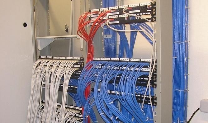 Baie réseau avec des câbles Ethernet rouge, blanc et bleu soigneusement connectés dans une salle serveur