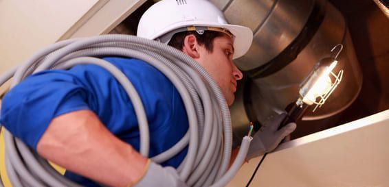 Ouvrier en uniforme bleu et casque blanc manipulant de grandes gaines métalliques dans un environnement industriel