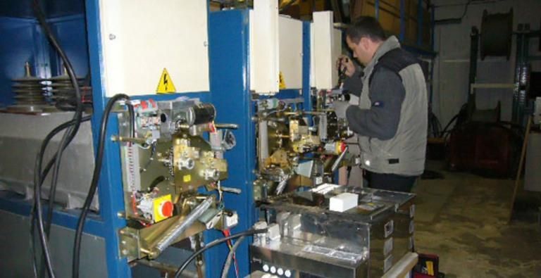 Un ouvrier inspecte des machines dans une usine, à côté d'une machine industrielle bleue.