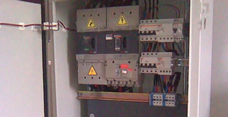 Panneau de commande électrique avec panneaux d'avertissement, disjoncteurs et câblage à l'intérieur d'une armoire.