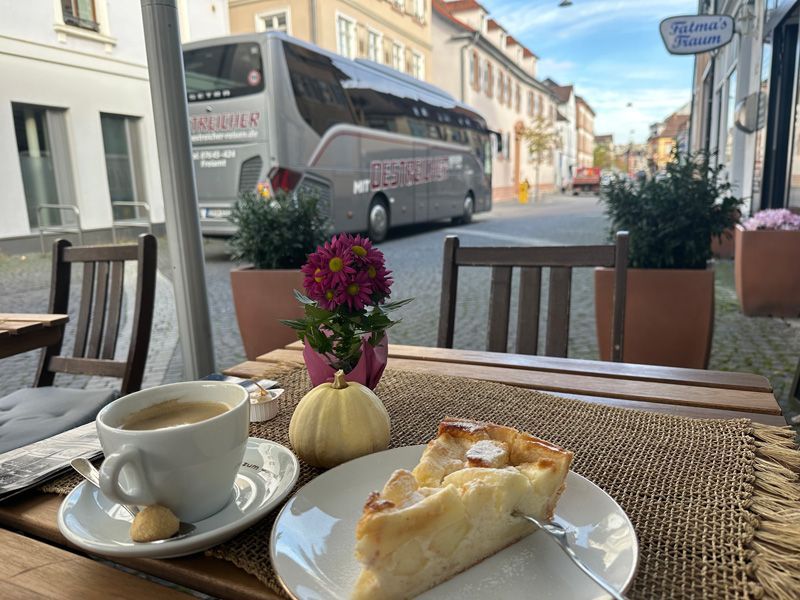 Szene in einem Straßencafé: Kaffee, Kuchen und ein Reisebus auf einer Kopfsteinpflasterstraße.