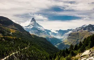Ein schneebedeckter Berg ist in einem Tal von Bäumen umgeben.