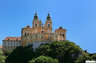 Auf einem Hügel steht ein großes Gebäude, umgeben von Bäumen.