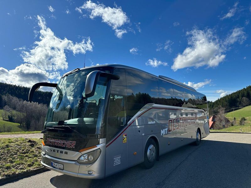 Grauer Reisebus parkt auf der Asphaltstraße, teils sonniger Tag.