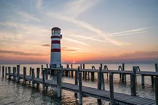 Ein Leuchtturm steht auf einem Holzsteg und überblickt den Ozean bei Sonnenuntergang.