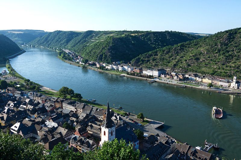 Der Rhein fließt durch eine Stadt, die eingebettet zwischen grünen Hügeln liegt.
