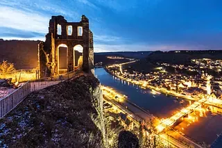 Eine Burg auf einem Hügel mit Blick auf einen Fluss bei Nacht.