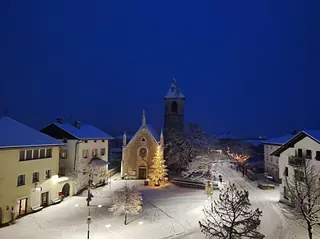 Eine Kirche mit einem Weihnachtsbaum davor ist von schneebedeckten Gebäuden umgeben.