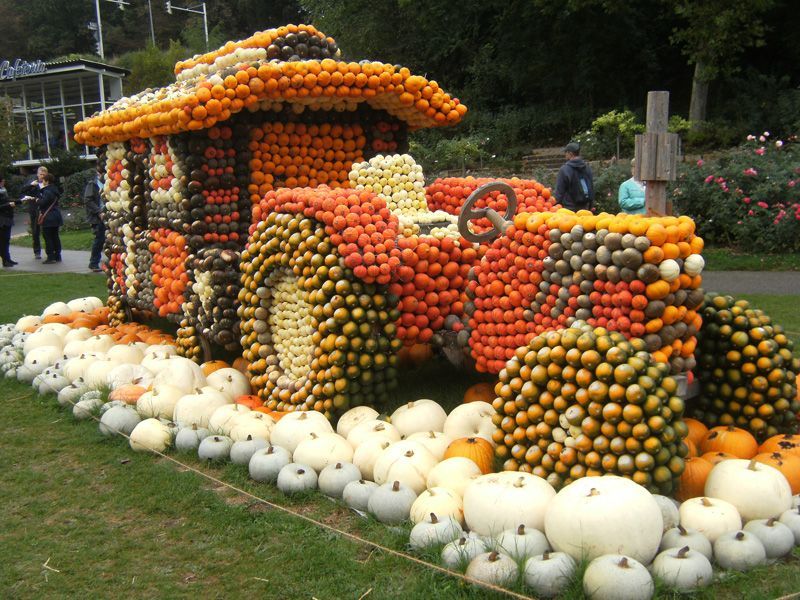 Eine Traktorskulptur aus Kürbissen in verschiedenen Farben, aufgestellt auf einer Rasenfläche, im Hintergrund sind Menschen zu sehen.