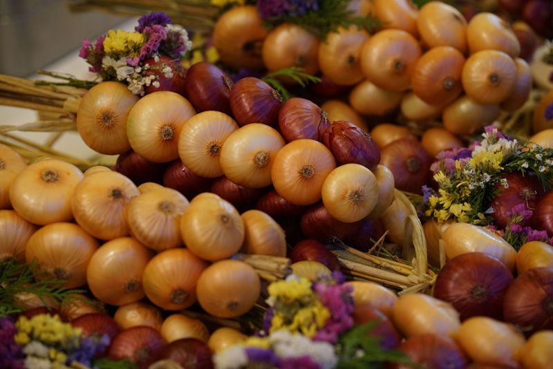 Bündel von gelben und roten Zwiebeln mit getrockneten Blüten, möglicherweise zum Verkauf auf einem Markt.