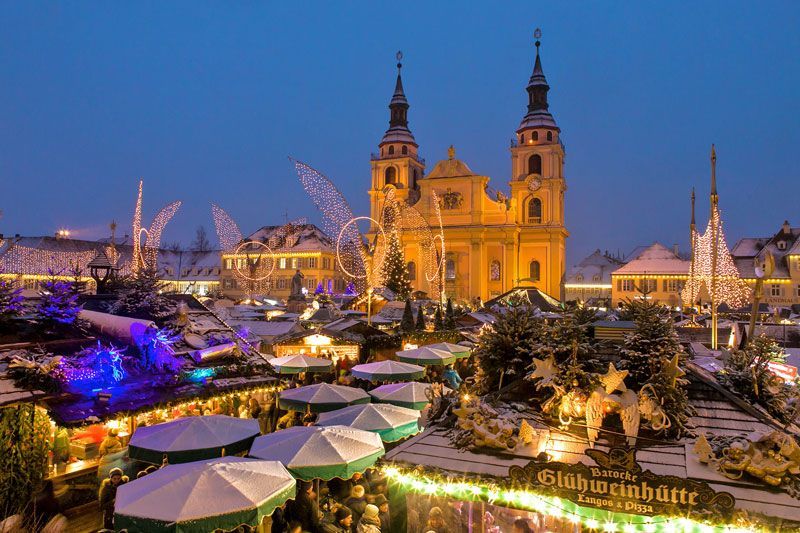 Weihnachtsmarkt, Deutschland, mit beleuchteten Ständen und Kirche in der Abenddämmerung.