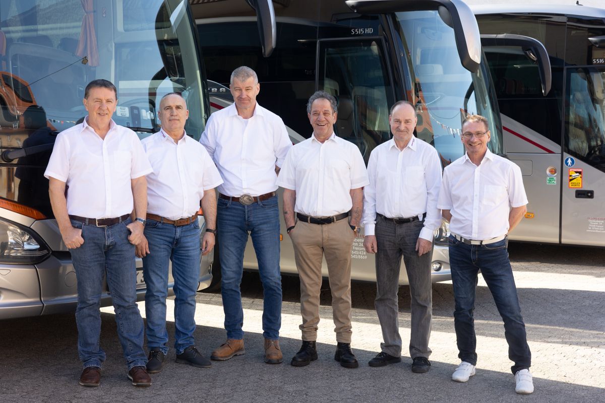 Eine Gruppe Männer posiert vor Bussen für ein Foto.