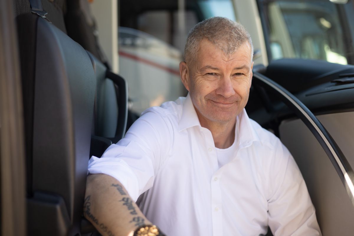 Ein Mann mit einer Tätowierung auf dem Arm sitzt auf dem Fahrersitz eines Lastwagens.