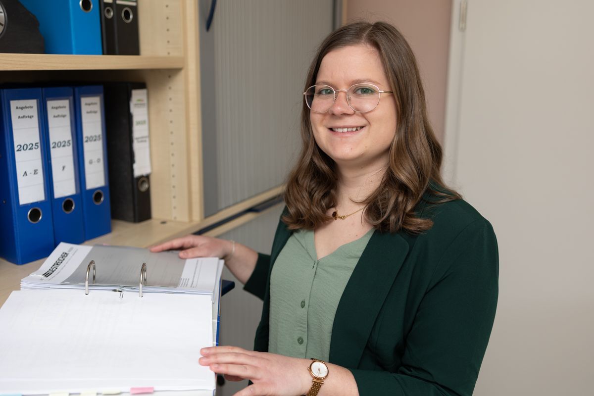 Eine Frau in einer grünen Jacke hält eine Schachtel Papier.