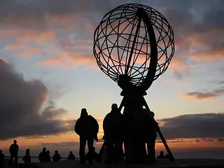 Eine Gruppe von Menschen steht bei Sonnenuntergang vor einem großen Globus.