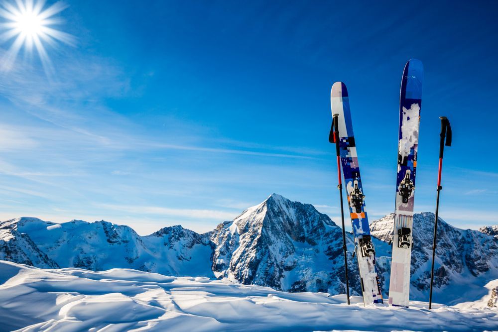Verschneiter Waldweg mit Skifahrern, die auf einer präparierten Piste zwischen schneebedeckten Bäumen gleiten.